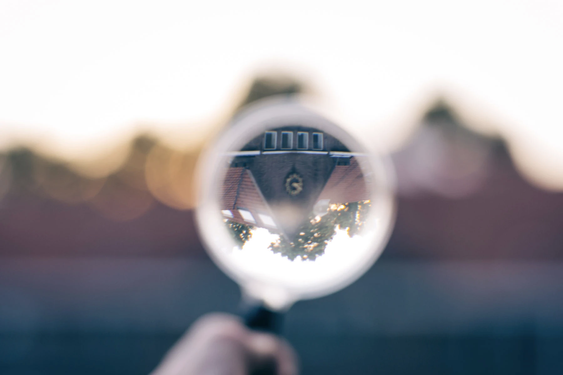 Photo of a building with a clock on it but it's turned upside down because I'm holding a magnifying glass in front of it. Such art.